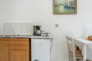 A compact kitchen with a sink, a small refrigerator, and a painting of boats on the wall. - Katerina's Studio '2' with Sea View and Private Balcony (Arginonta)