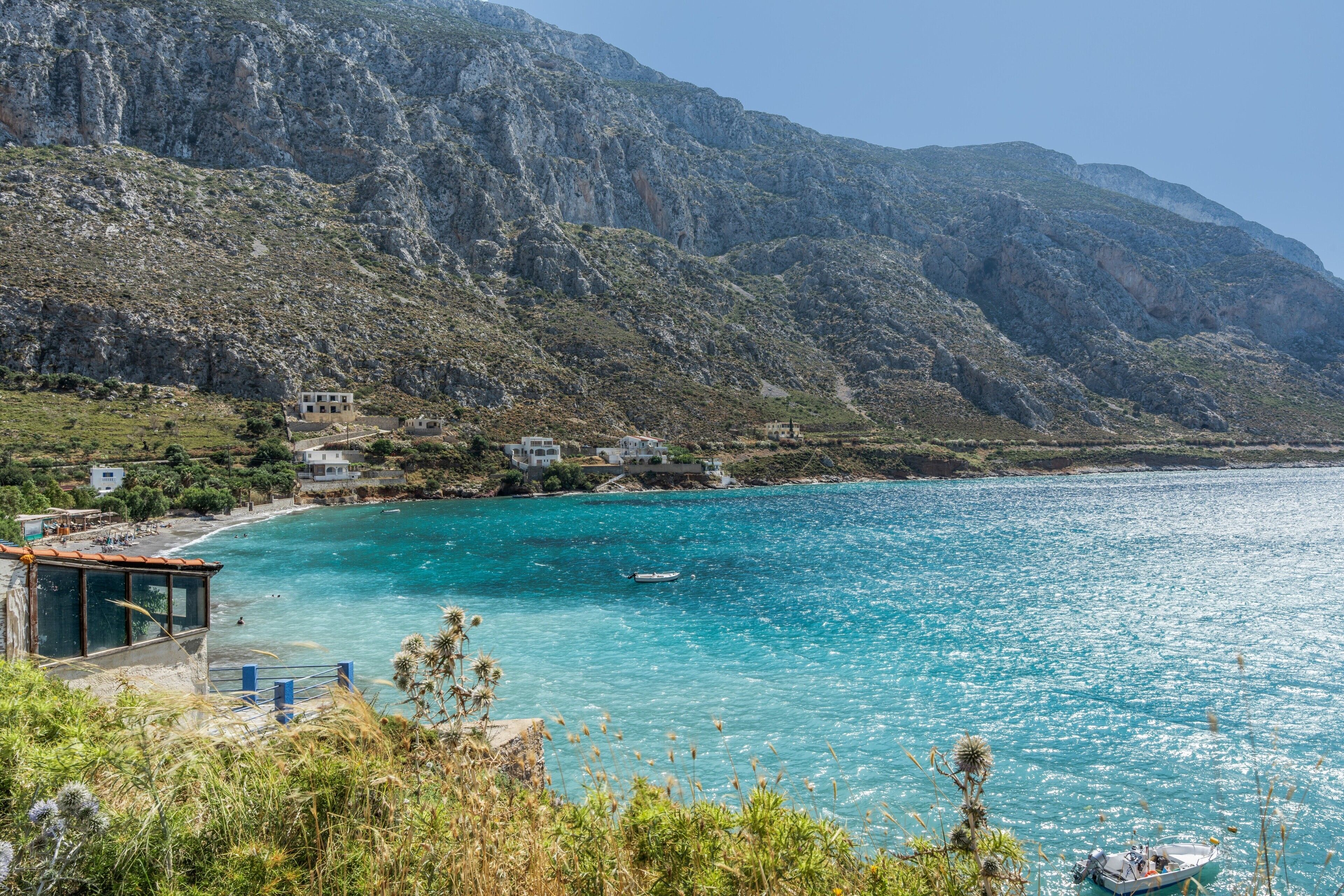 Une vue sur la côte, avec des montagnes en arrière-plan, une mer turquoise et limpide, et un petit bateau.