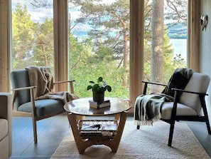 Ein Zimmer mit großem Fenster, zwei Stühlen, einem kleinen runden Tisch und einem Blumentopf.