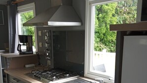 A modern kitchen with a gas stove, stainless steel sink, and a window overlooking greenery. - Mobile Home “Home” with Private Terrace (Plounévézel)