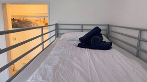 A single bed with white bedding, a metal headboard, and a view of the beach through an open door. - Large oasis on Langeoog (Langeoog)