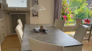 Un comedor con una mesa, sillas, una lámpara y vistas a un jardín con flores.