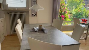 A dining area with a table, chairs, a lamp, and a view of a garden with flowers. - Large oasis on Langeoog (Langeoog)