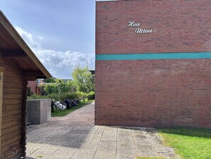 A brick building with a sign reading 'Hus Utters' and a covered walkway leading to a parking area with bicycles. - Large oasis on Langeoog (Langeoog)