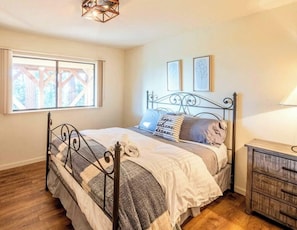A bedroom with a metal bed frame, a wooden dresser, a window with a view, and two framed pictures on the wall.