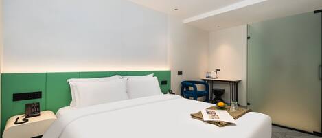 Habitación de hotel con cama, escritorio con silla, teléfono y una mesita con frutero y vaso.