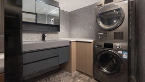 A modern laundry room with a built-in washer and dryer, a large mirror above the sink, and a marble backsplash. - Key View Hotel (Chongqing)