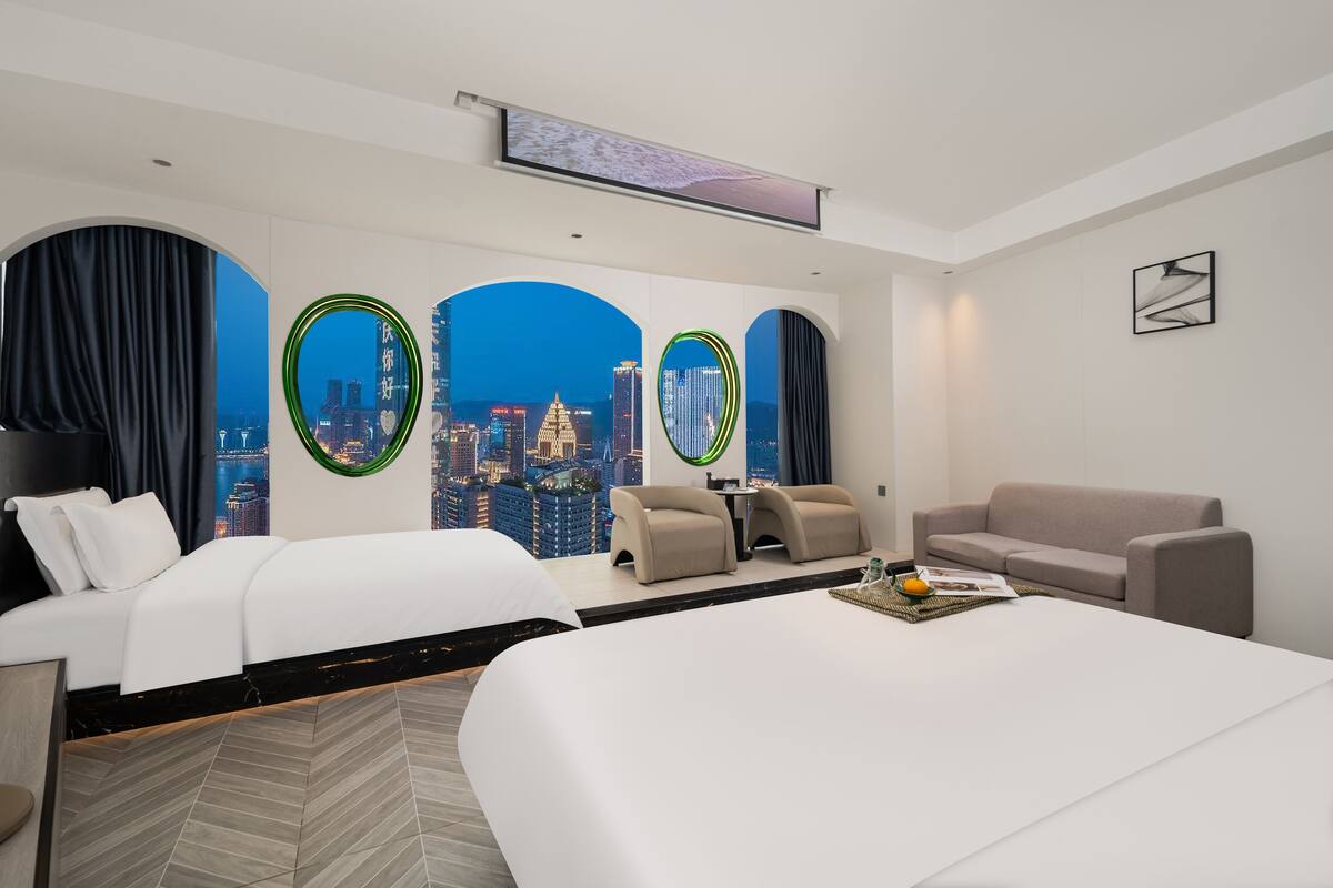 A hotel room with a city view, a bed, two sofas, a coffee table, and a TV.