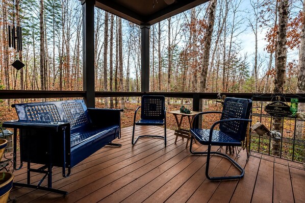 A covered outdoor deck with a wooden floor, a blue sofa, two chairs, and a small table.