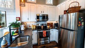 A modern kitchen with stainless steel appliances, white cabinetry, and a wooden floor. - Cozy Cabin Retreat with Loft Hideaway, Fire Pit & Nature Trails in Monteagle, Tennessee (Monteagle)