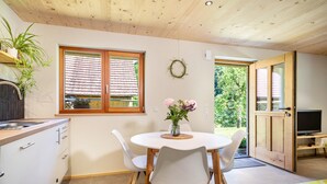 Eine moderne Küche mit weißen Schränken, einer Holzbalkendecke und einem Essbereich mit rundem Tisch und weißen Stühlen.