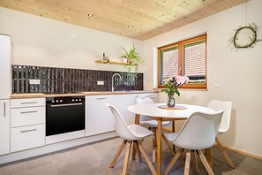 Eine moderne Küche mit weißen Schränken, einer schwarzen Fliesenrückwand, Holzboden und einem Essbereich mit weißen Stühlen und einem runden Tisch.