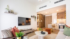 Ein modernes Wohnzimmer mit Flachbildfernseher, Sofa, Couchtisch und einem im Hintergrund sichtbaren Küchenbereich.