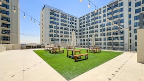 A rooftop terrace with outdoor seating, a grill, and string lights. - Stylish 1BR Just Steps from Town Square Park, Minutes Drive to Miracle Garden (Dubai)