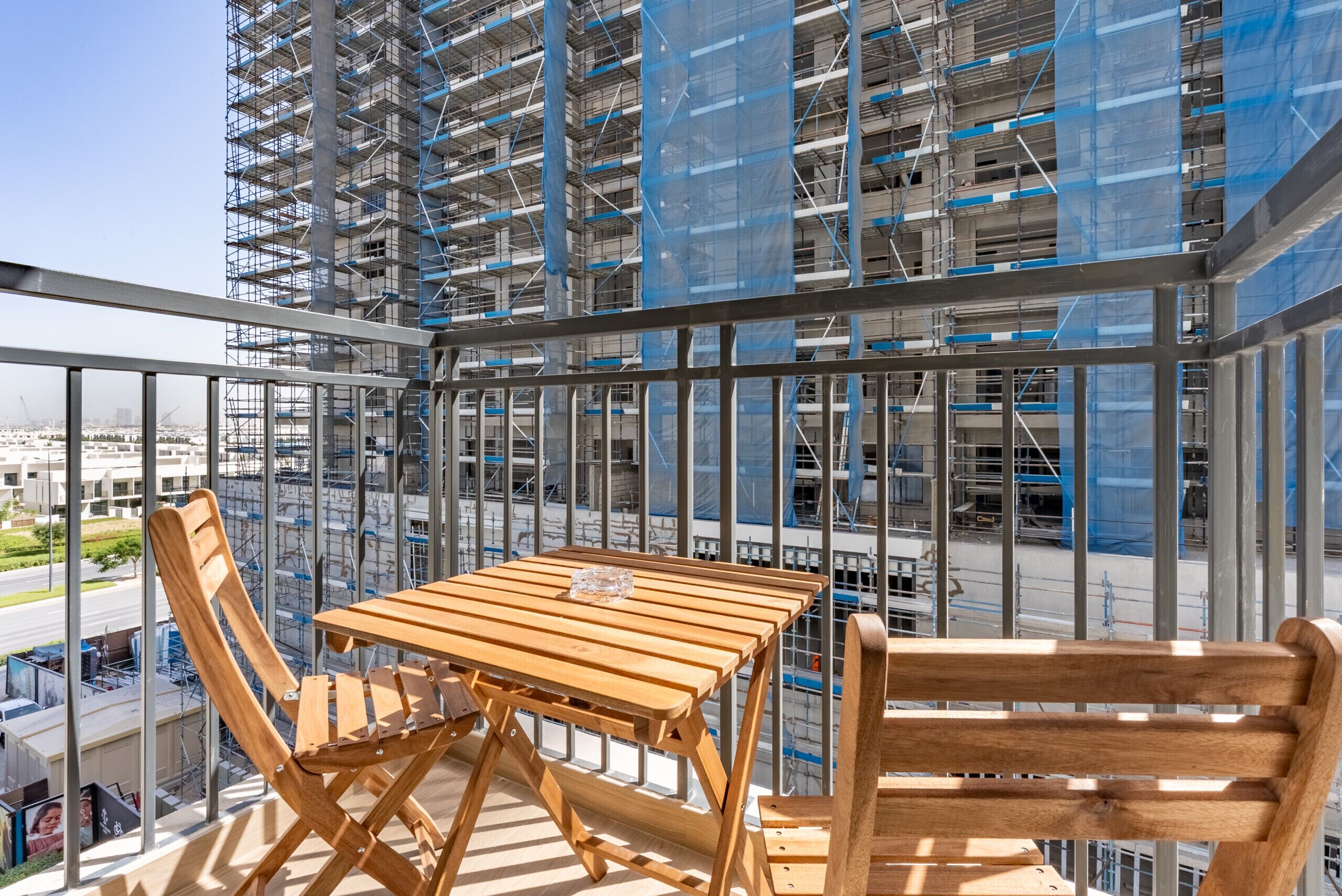 A balcony with a wooden table and chairs, overlooking a construction site with scaffolding.