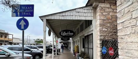 A street view with a Texas Hill Country Trail sign, a Kaffe Haus restaurant, parked cars, and a stone building facade.