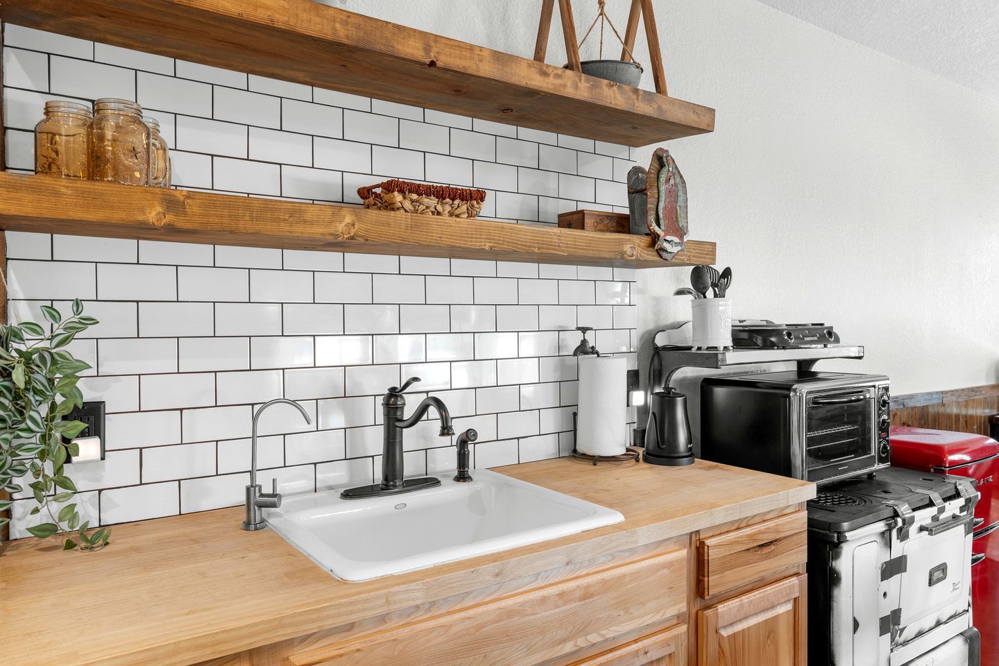 A kitchen with a white sink, wooden countertop, and a red toaster oven.