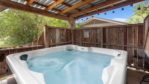 Ein Whirlpool unter einer Holzw pergola mit Metallveranda, umgeben von einem Holzzaun.