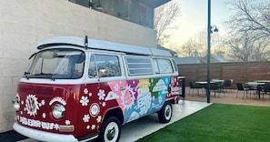 A vintage VW bus parked in a covered outdoor area with tables and chairs. - Chic, Renovated Barn with Hot Tub near the Heart of Fredericksburg Texas, Perfect for a Rustic Escape (Fredericksburg)