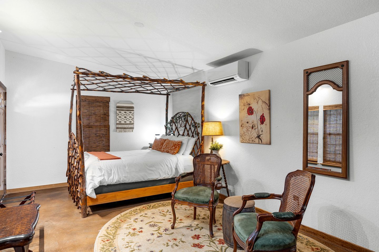 A four-poster bed with a canopy, a round rug with floral patterns, and two upholstered chairs.