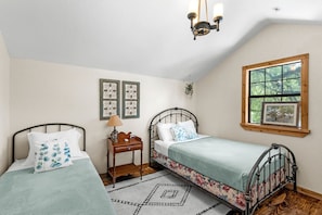 A bedroom with two single beds, a nightstand, a wall-mounted lamp, and a window with a view of trees. - Chic, Renovated Barn with Hot Tub near the Heart of Fredericksburg Texas, Perfect for a Rustic Escape (Fredericksburg)