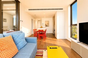 A modern living room with a sofa, a dining table, and a TV. - Stylish Apartment Near Macquarie Uni & Metro (Macquarie Park)