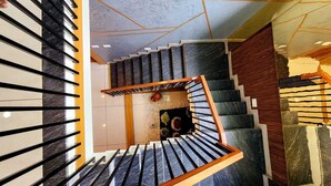 A modern staircase with a wooden handrail and black steps, leading to a landing with a decorative wall and a small plant. - Neelambari Estate Stay (Madikeri)