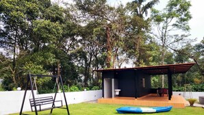 A covered outdoor area with a swing set, a small building with a toilet, and a blue boat. - Neelambari Estate Stay (Madikeri)