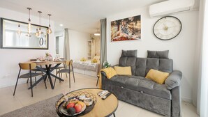 A modern living room with a grey sofa, a dining table with chairs, a coffee table with fruit, and a large mirror. - Vacation Apartment 'Infinity Summer' with Mountain View, Wi-Fi and Air Conditioning (Amarilla Golf)