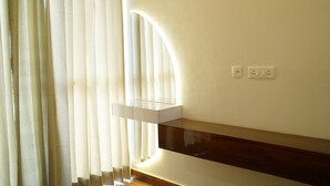 A modern bathroom with a wooden vanity, a glass shelf, and a white wall with two electrical outlets. - Harmony Haven: Luxurious 3BHK Haven for All. (Sahibzada Ajit Singh Nagar)