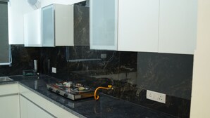 A kitchen with white cabinets, a black countertop, and a gas stove. - Harmony Haven: Luxurious 3BHK Haven for All. (Sahibzada Ajit Singh Nagar)