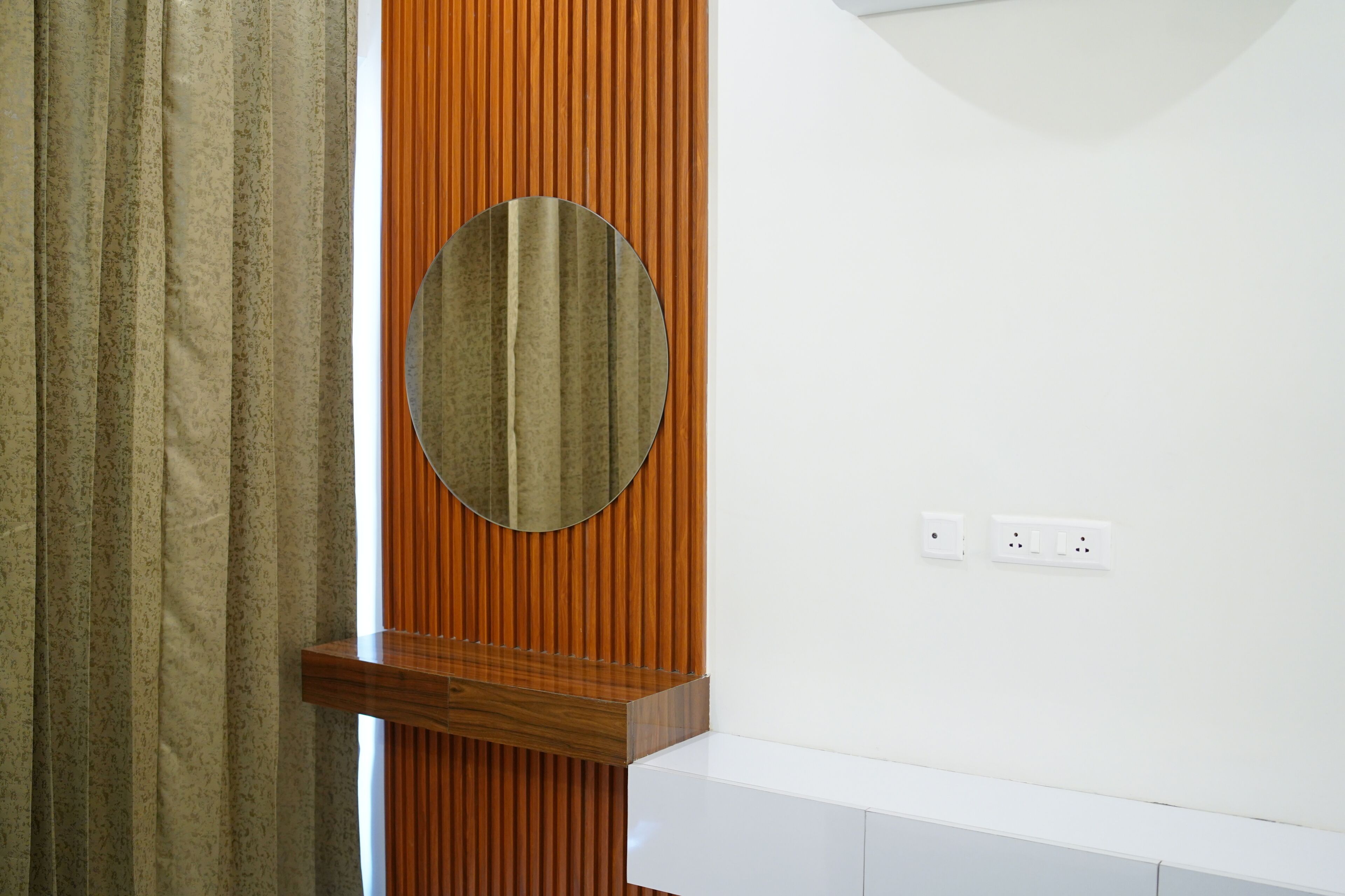 Un baño con tocador de madera, espejo redondo y encimera blanca.