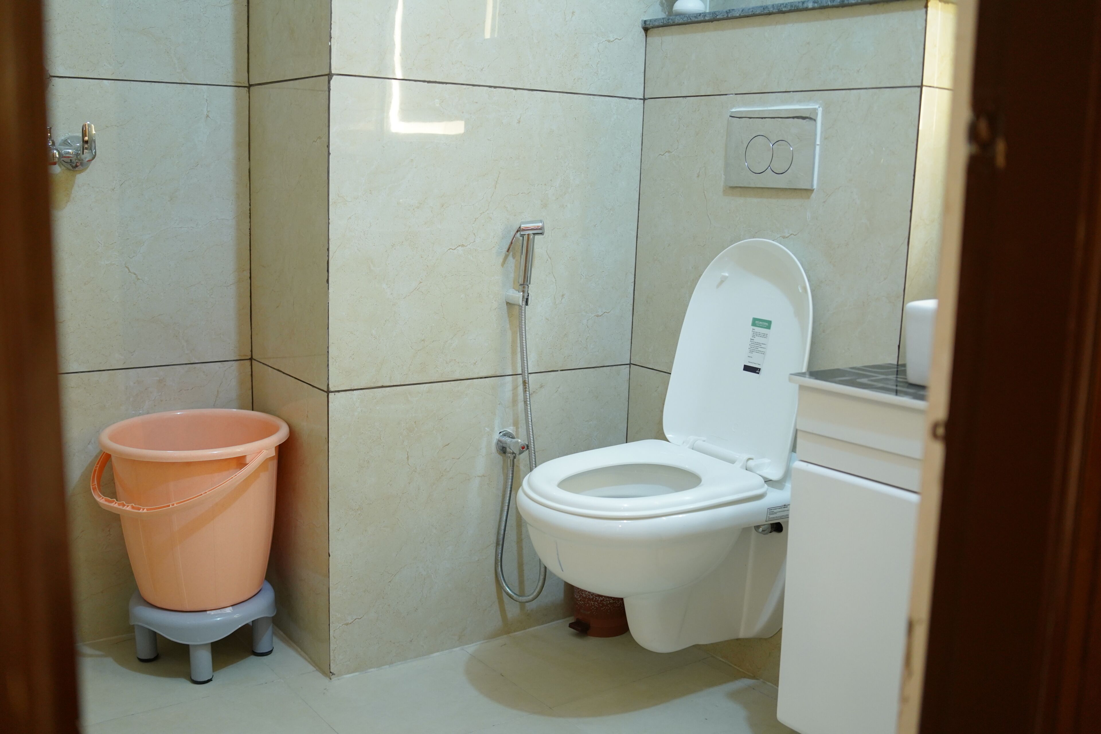 Ein kleines Badezimmer mit Toilette, Dusche und einem pinken Eimer auf einem Hocker.