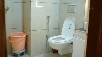 Ein kleines Badezimmer mit Toilette, Dusche und einem pinken Eimer auf einem Hocker.