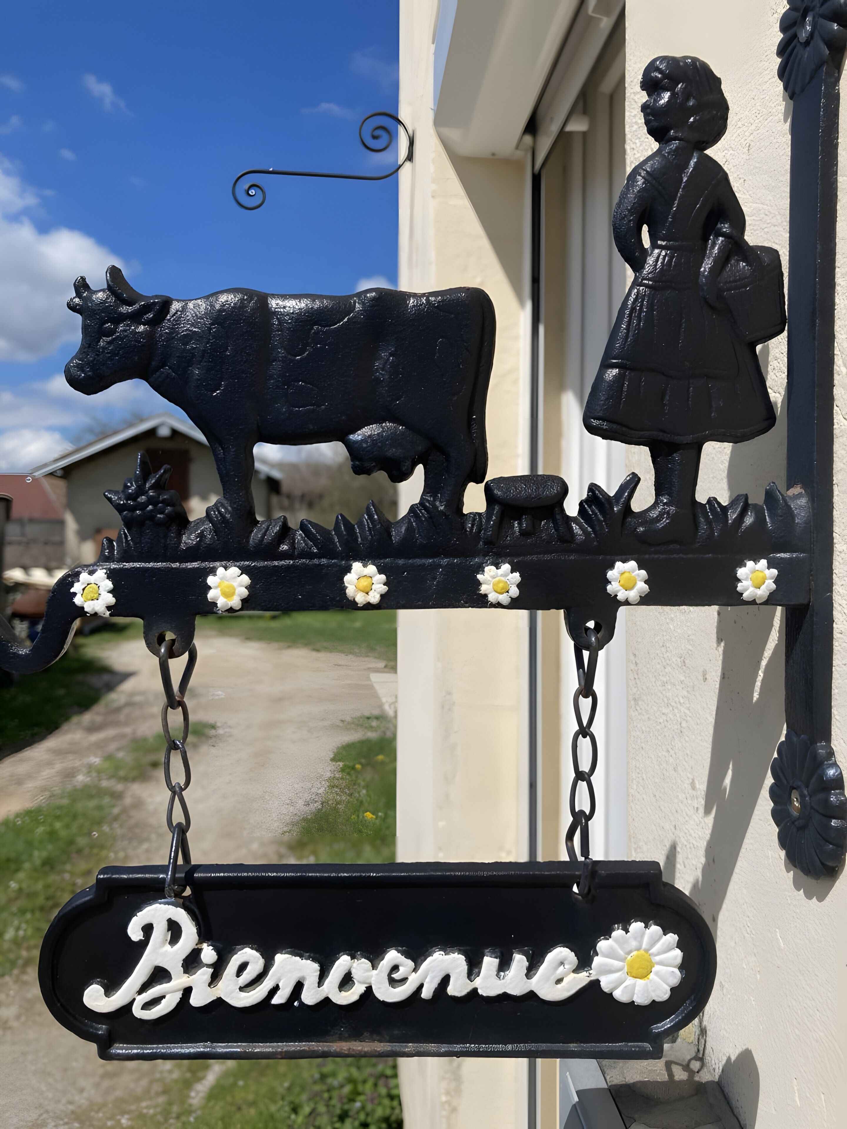 A black metal sign with a cow and a girl, and the word 'Bienvenidos' on a building.