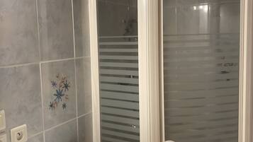 Een badkamer met douchecabine, een haardroger en een betegelde wand met bloemendesign.