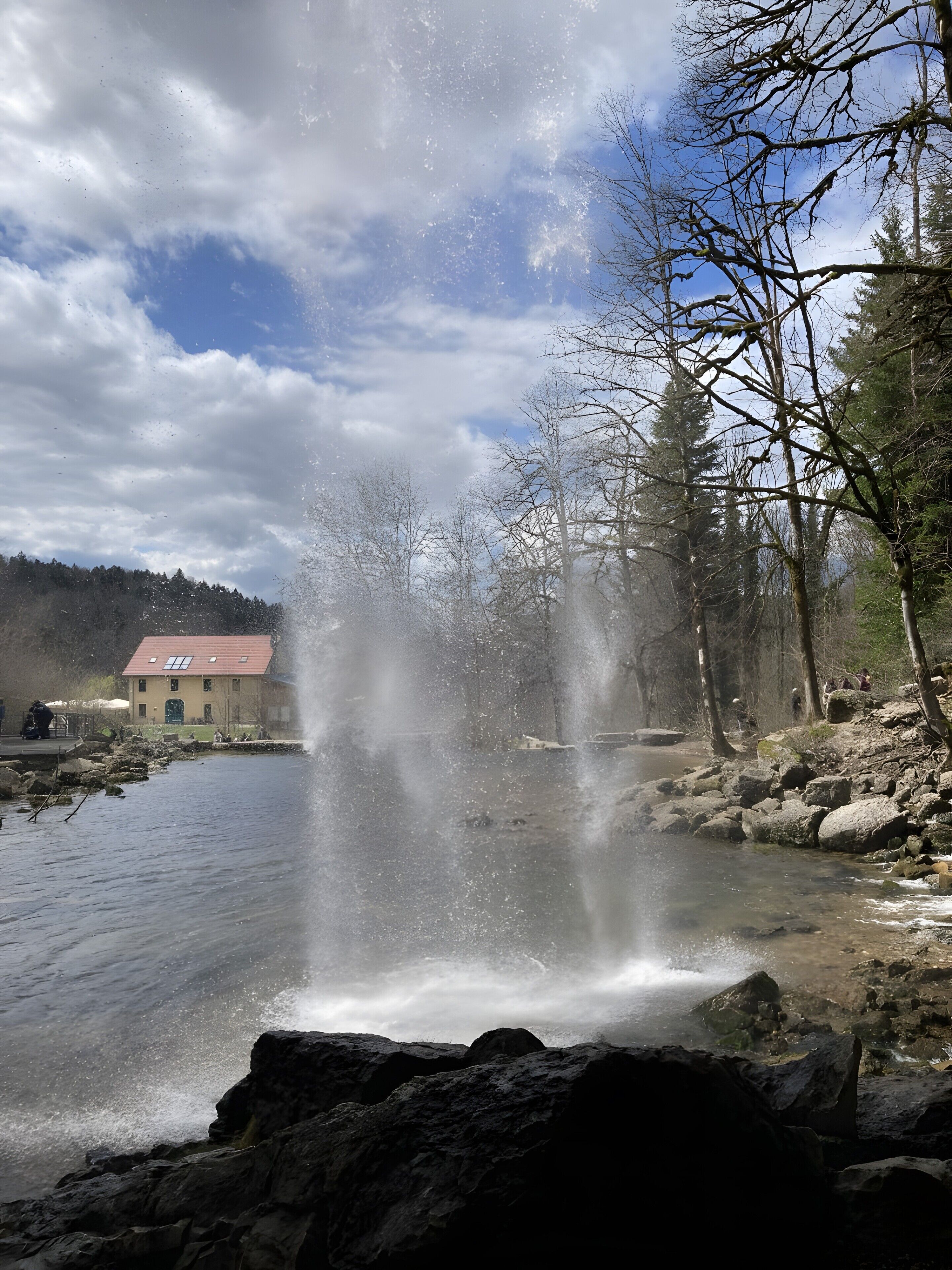 A natural landscape with a waterfall, a building with a red roof, and a forested area.