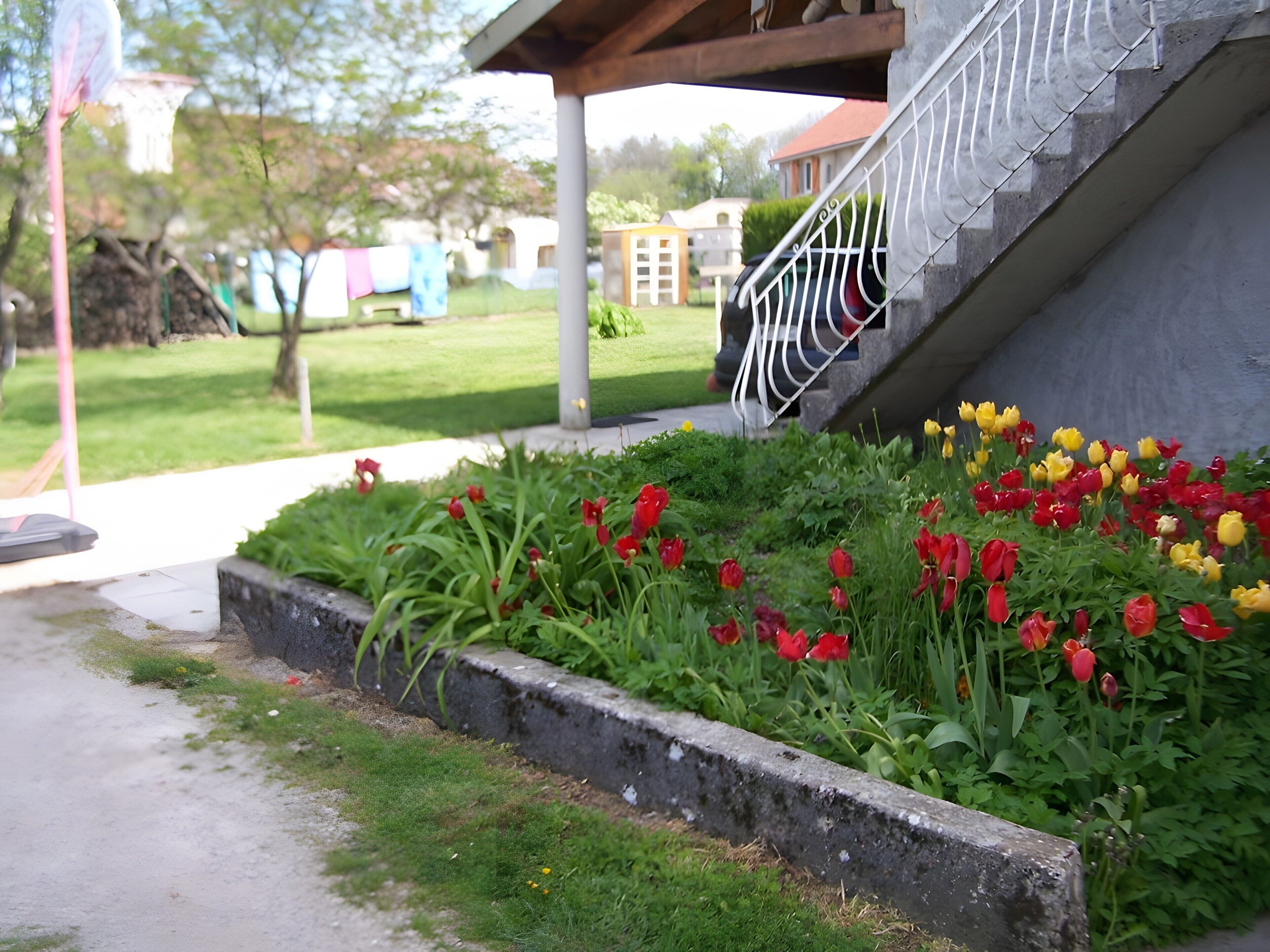 A garden with red and yellow tulips, a concrete planter, and a building with a staircase.