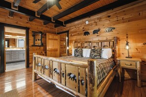 A wooden cabin interior with a bed, a nightstand, and a kitchen area. - New Listing!  Hot Tub, Game Room, Theater, Close to Town + Free Tickets (Gatlinburg)