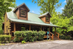 A log cabin with a green metal roof, a porch, and a staircase leading to the entrance. - New Listing!  Hot Tub, Game Room, Theater, Close to Town + Free Tickets (Gatlinburg)