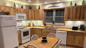 A kitchen with wooden cabinets, a white refrigerator, a microwave, a stove, a sink, and a dining table with chairs. - Amazing hilltop views of gorgeous Sage Lake with beach and boat launch access. (Hale)