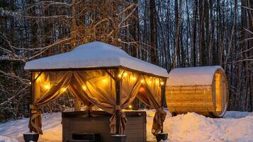 A wooden cabin with a snow-covered roof and a large cylindrical structure, surrounded by a snowy forest.