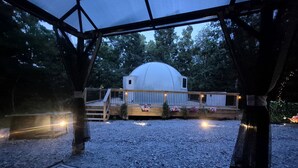 Un espace extérieur abrité doté d’une structure en forme de dôme, d’un sol en gravier et d’une terrasse en bois avec des garde-corps.