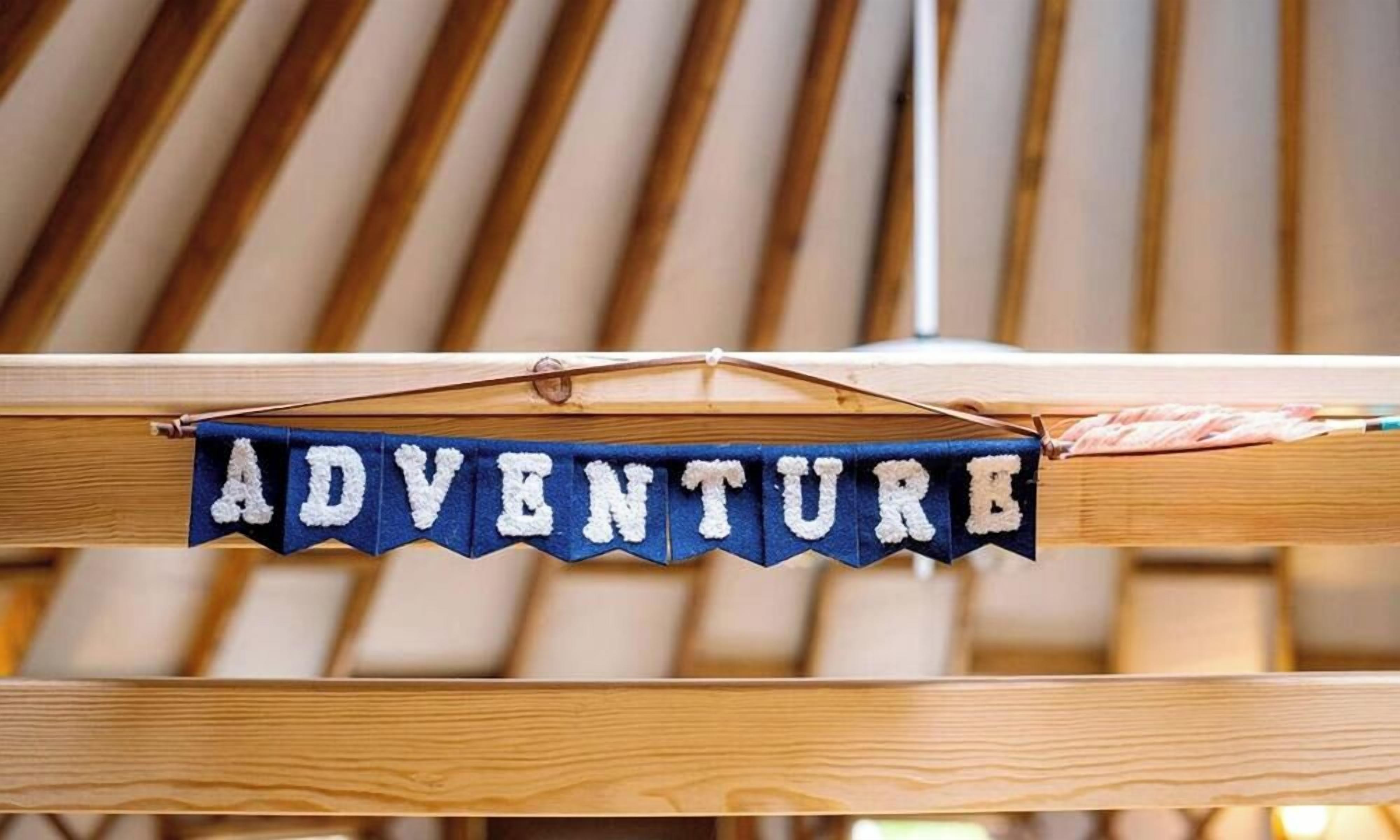 Een houten stoel met een blauwe banner die over de rug hangt, waarop 'ADVENTURE' staat.