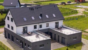 Una casa moderna de dos pisos con techo plano, ventanas amplias y un balcón con mobiliario exterior.