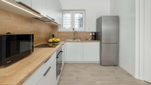 Una cocina moderna con armarios blancos, un refrigerador de acero inoxidable, horno empotrado y encimera de madera.