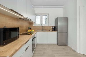 Eine moderne Küche mit weißen Schränken, einem Edelstahl-Kühlschrank, einem eingebauten Backofen und einer Holzarbeitsplatte.