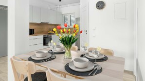 Un comedor moderno con una mesa de madera preparada para cuatro personas, un jarrón de tulipanes y una cocina al fondo.