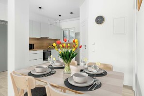 Ein moderner Essbereich mit einem Holztisch, gedeckt für vier Personen, einer Tulpenvase und einer Küche im Hintergrund.