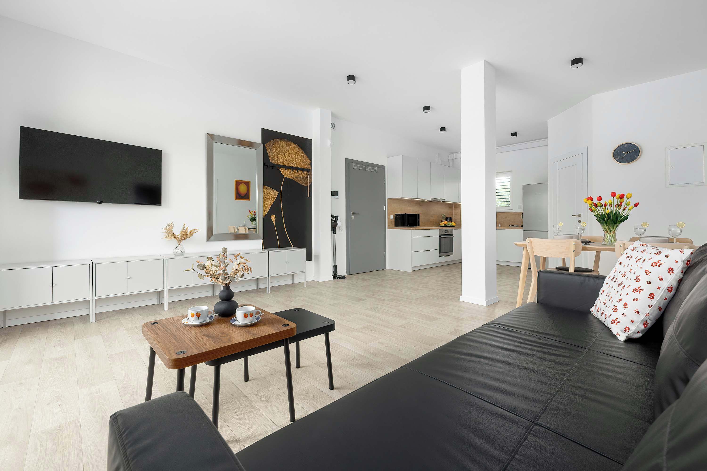 A modern living area with a black sofa and wooden coffee table. The apartment has an open and comfortable layout.